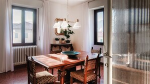 A dining area with a wooden table, chairs, a chandelier, and a view through a window. - STELLA APARTMENT  (Como)