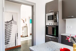 Una cocina moderna con horno empotrado y microondas, encimera de mármol y vistas al comedor.