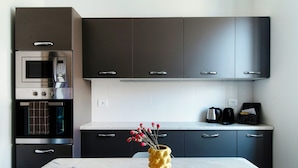 A modern kitchen with dark cabinets, a built-in oven, and a marble countertop. - STELLA APARTMENT  (Como)