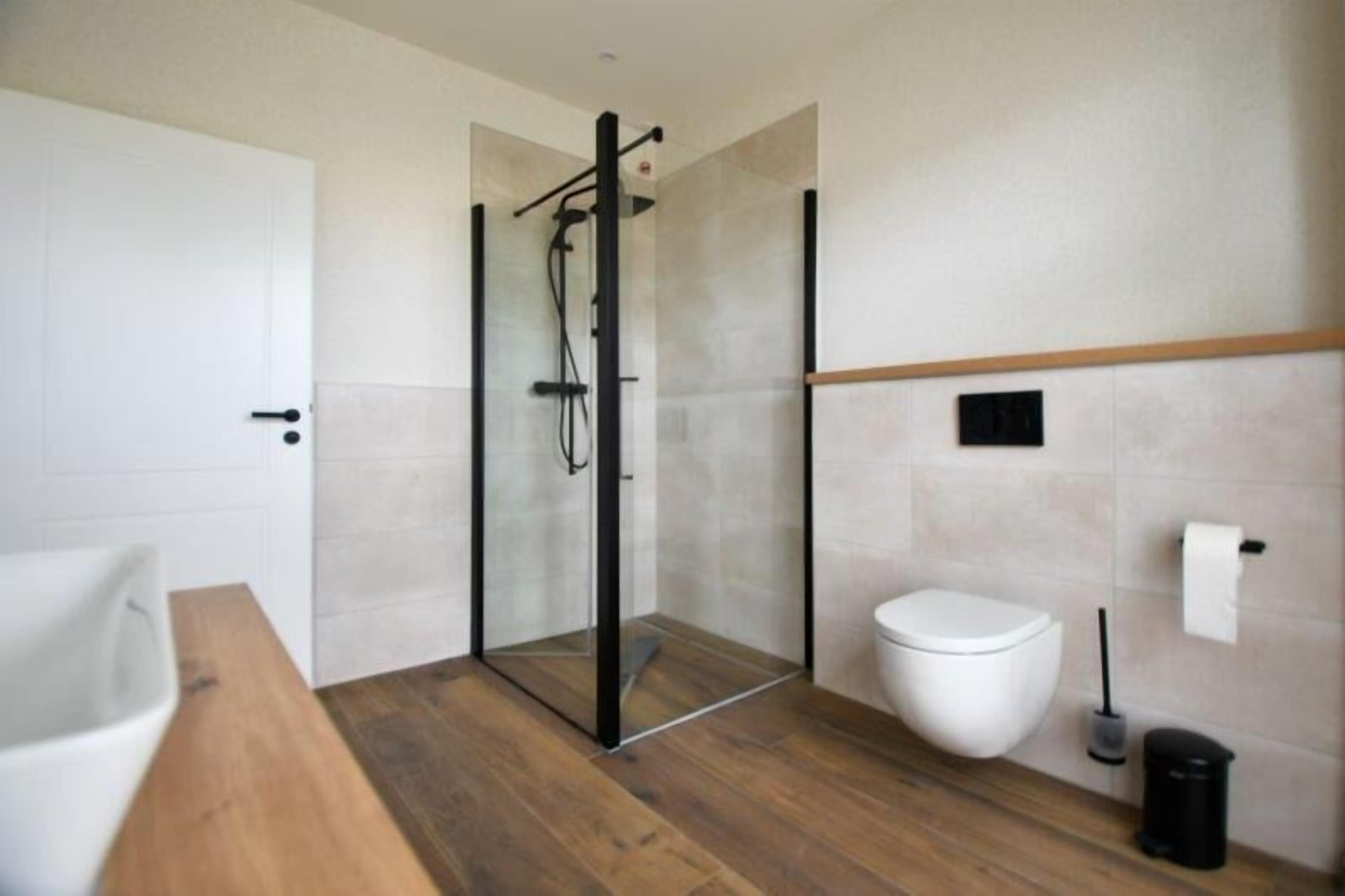A modern bathroom with a glass shower enclosure, a toilet, and a wooden vanity.