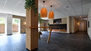 Un hall d’entrée spacieux au design moderne, agrémenté d’une colonne en bois ornée de plantes, de deux lampes suspendues orange et d’un espace détente avec des fauteuils.