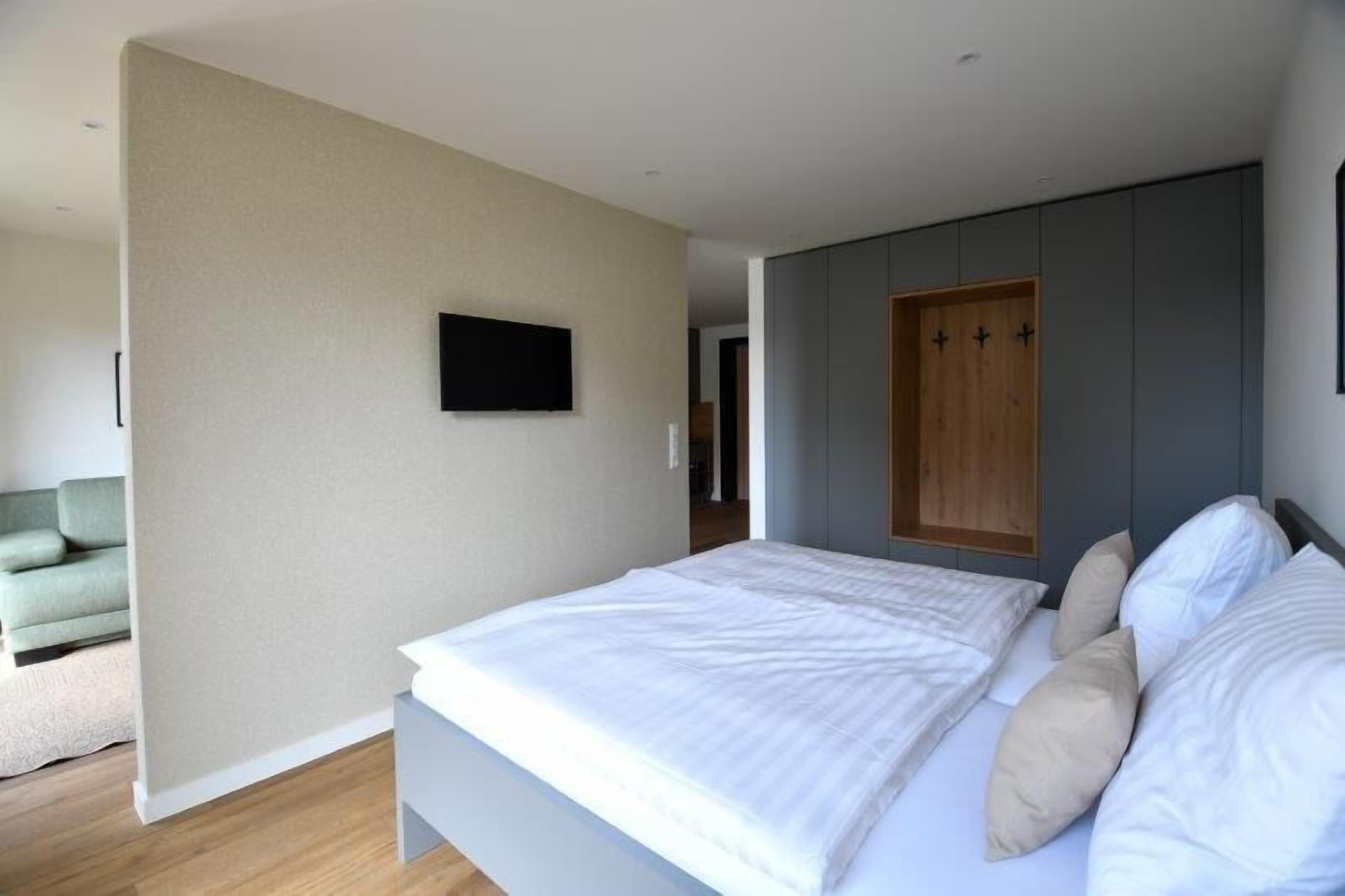 A modern bedroom with a large bed, a flat-screen TV mounted on the wall, and a wooden wardrobe.