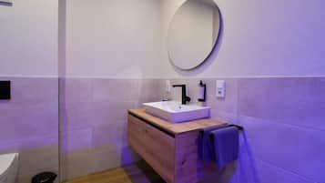 Een moderne badkamer met een witte wasbak, een houten opbergmeubel en een ronde spiegel.