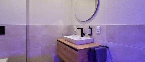 A modern bathroom with a white sink, wooden vanity, and a round mirror.