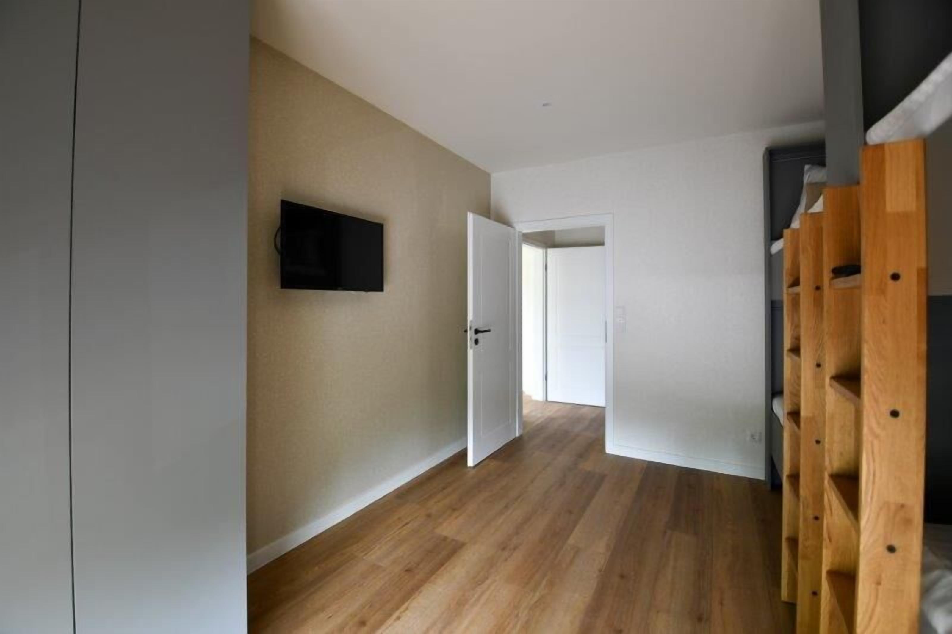 Un pasillo con piso de madera, una puerta blanca y un televisor montado en la pared.
