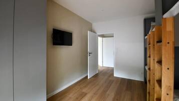 Un pasillo con piso de madera, una puerta blanca y un televisor montado en la pared.