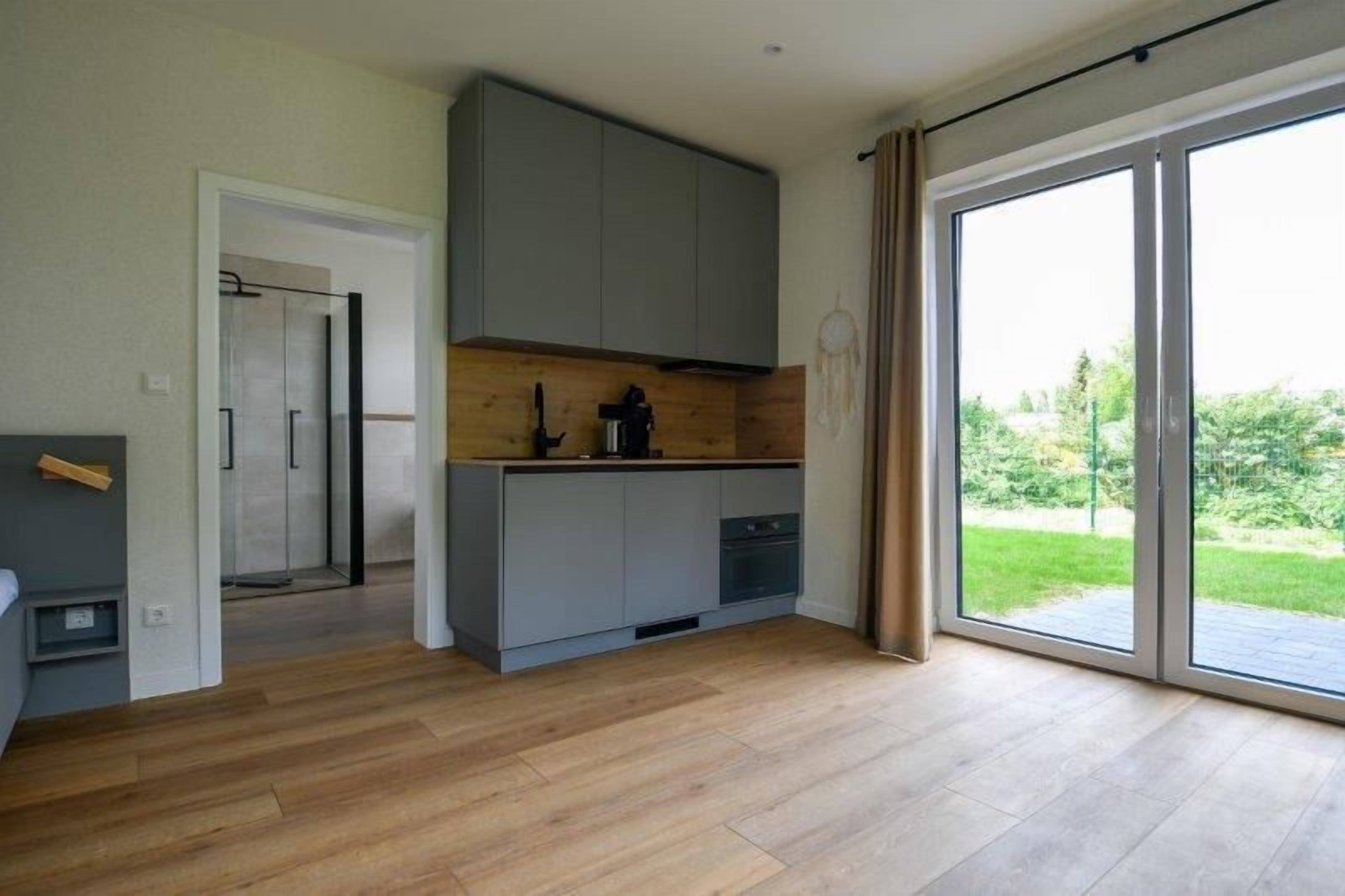 A modern kitchen with grey cabinets, a wooden countertop, and a view of a green landscape through large sliding glass doors.