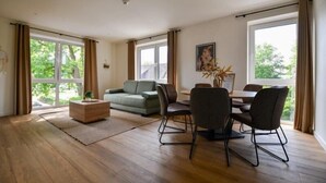 Une pièce spacieuse avec un plancher en bois, un canapé vert, une table à manger avec des chaises et de grandes fenêtres avec des rideaux.