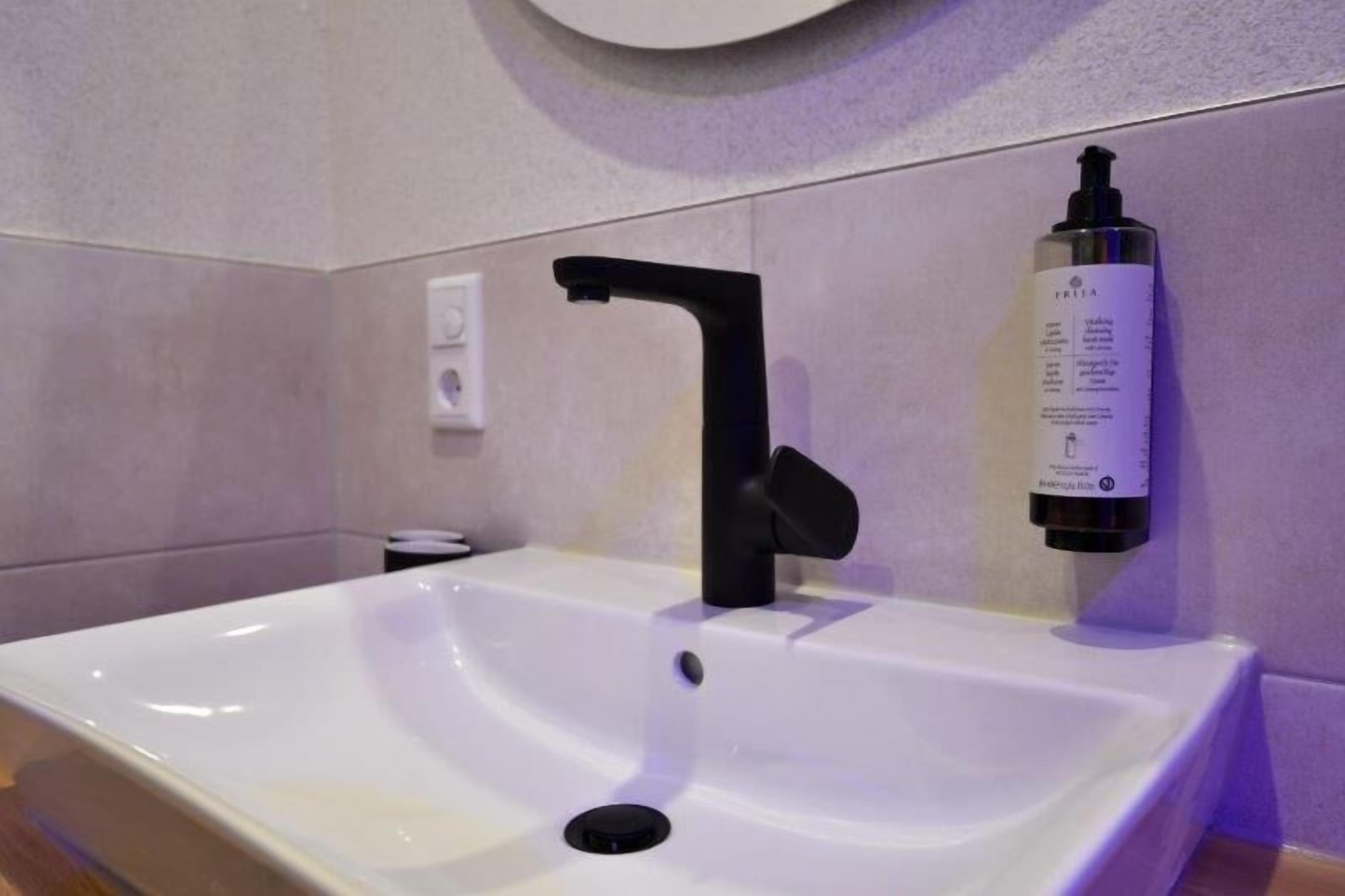 Un baño moderno con un lavamanos blanco, grifo negro y una botella de jabón de manos en la pared.