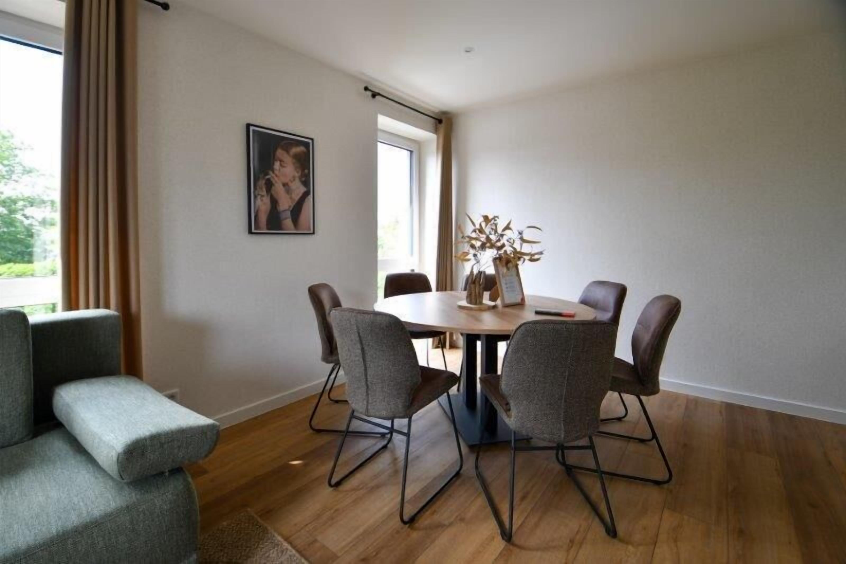 Un espace repas moderne avec une table ronde et six chaises, un canapé et une fenêtre avec des rideaux.
