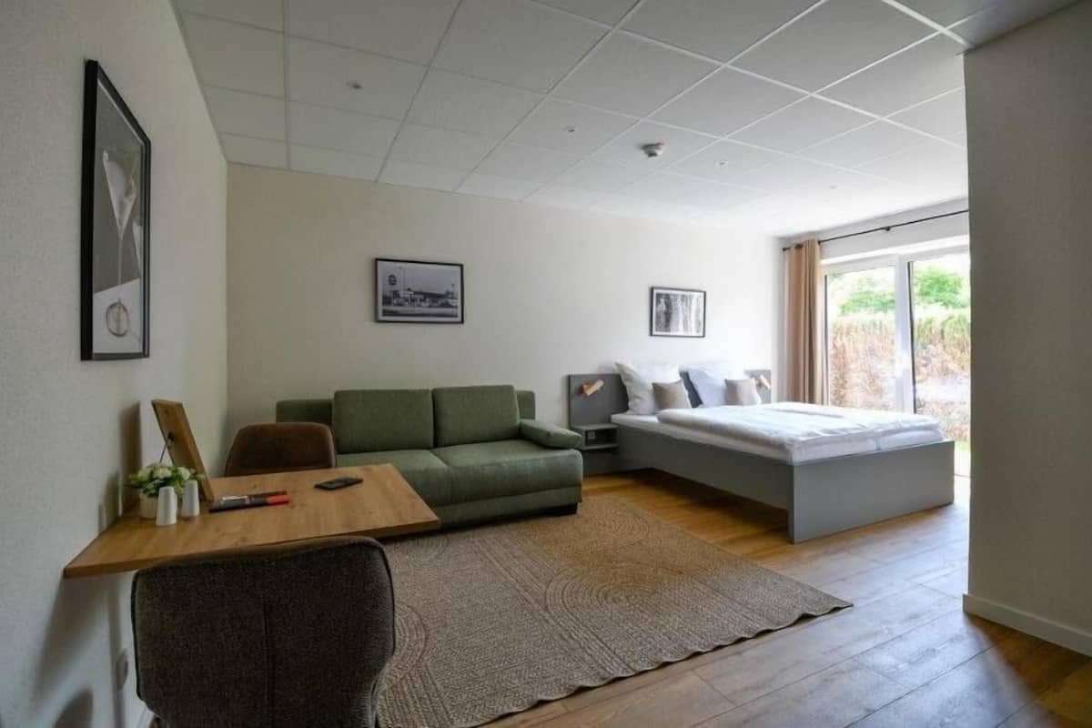 A modern bedroom with a green sofa, a wooden desk, and a bed with a grey headboard.