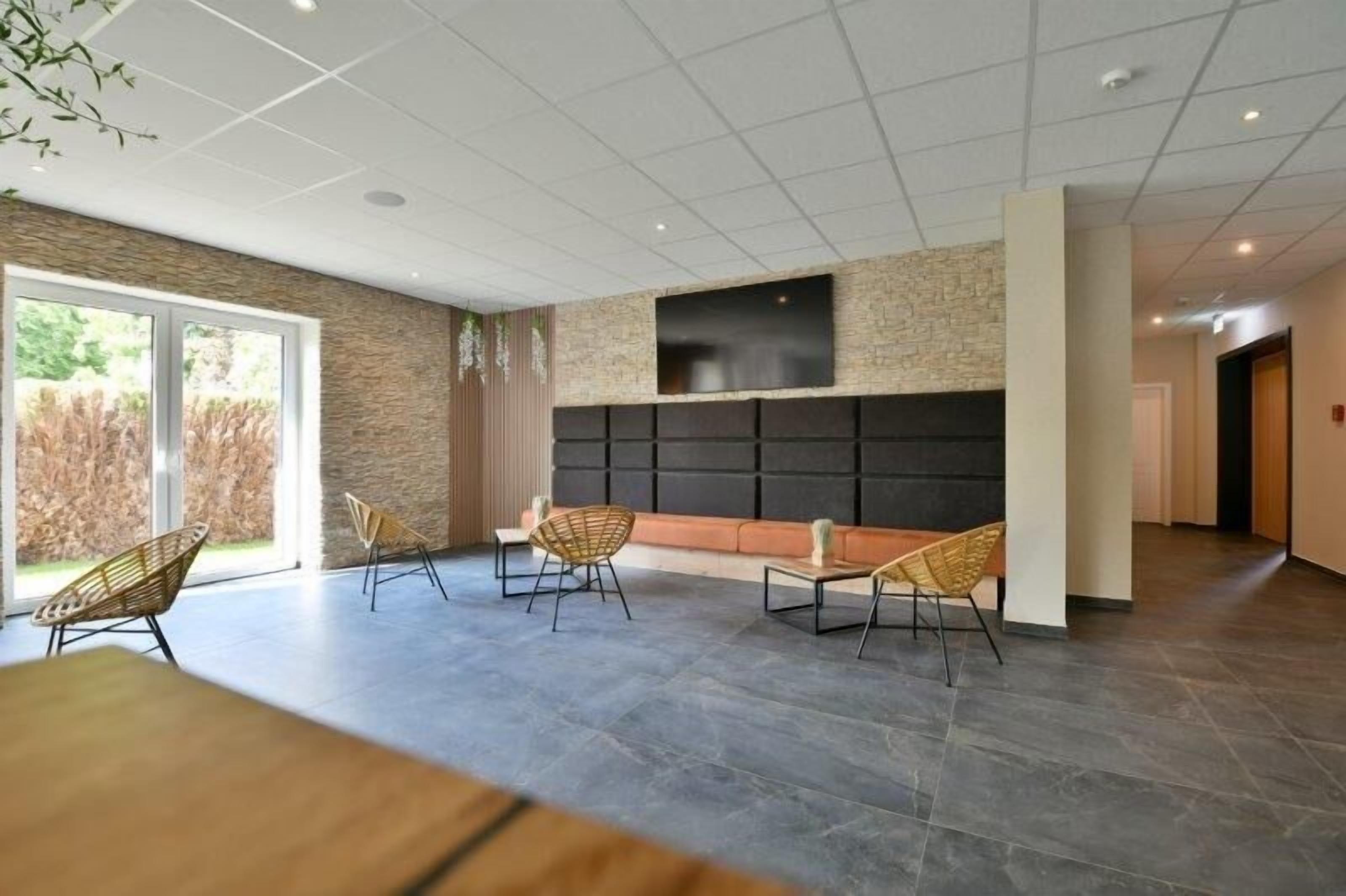 A modern lobby with a stone wall, a flat-screen TV, and wicker chairs.