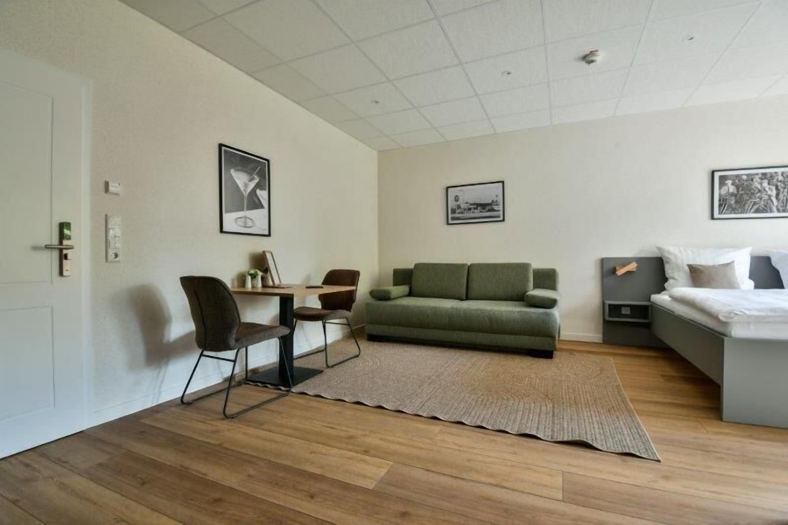 A modern room with a green sofa, a small table with chairs, a bed, and two framed pictures on the walls.