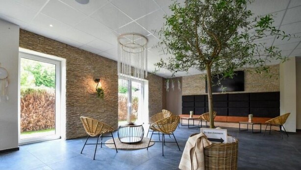 Un intérieur moderne avec un mur en pierre, un grand arbre, des meubles en osier et un téléviseur à écran plat.