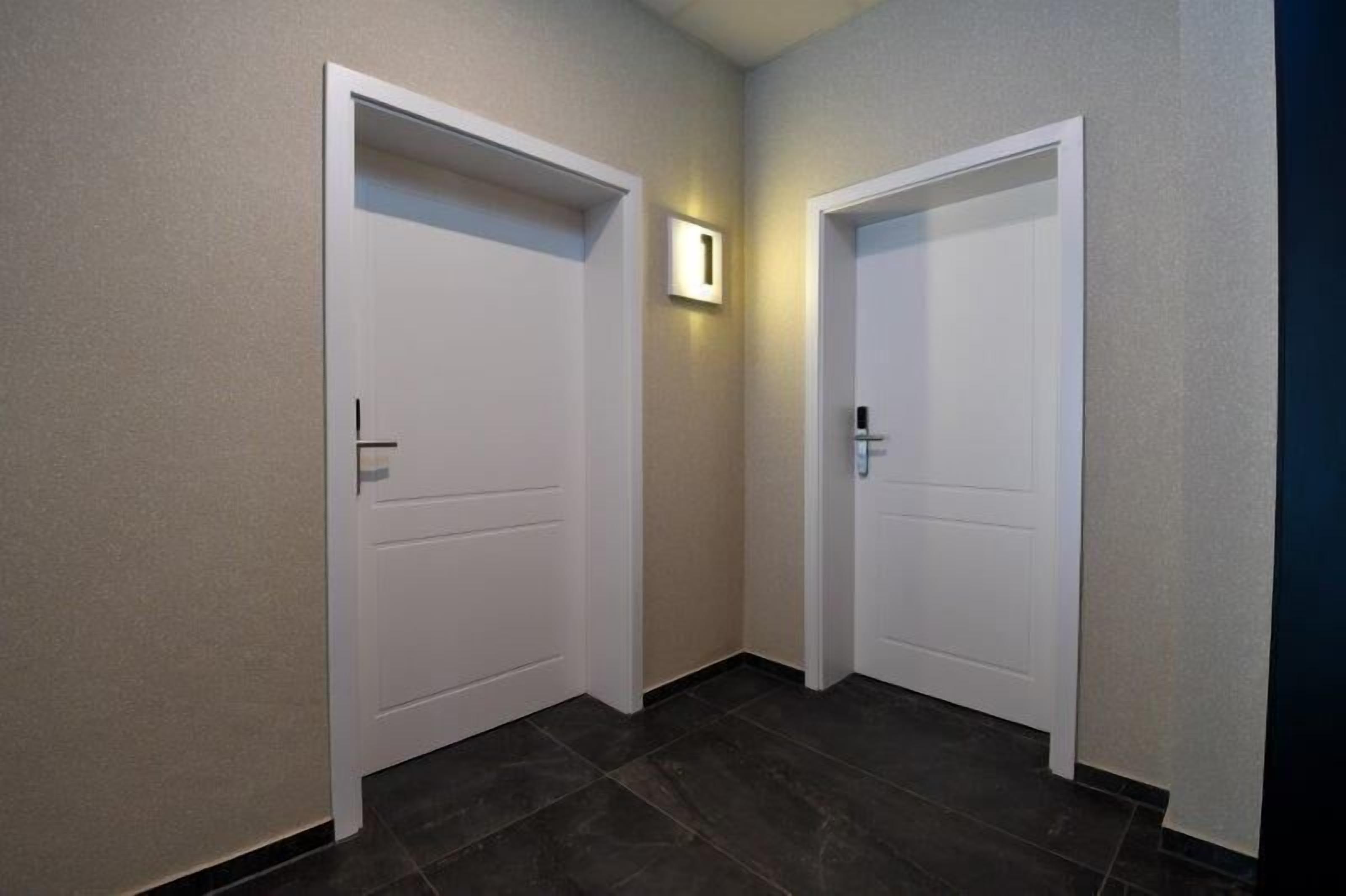 A hallway with two white doors, one with a light switch above it, and dark tiled flooring.