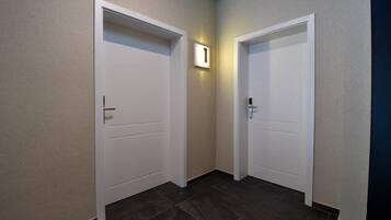 A hallway with two white doors, one with a light switch above it, and dark tiled flooring.