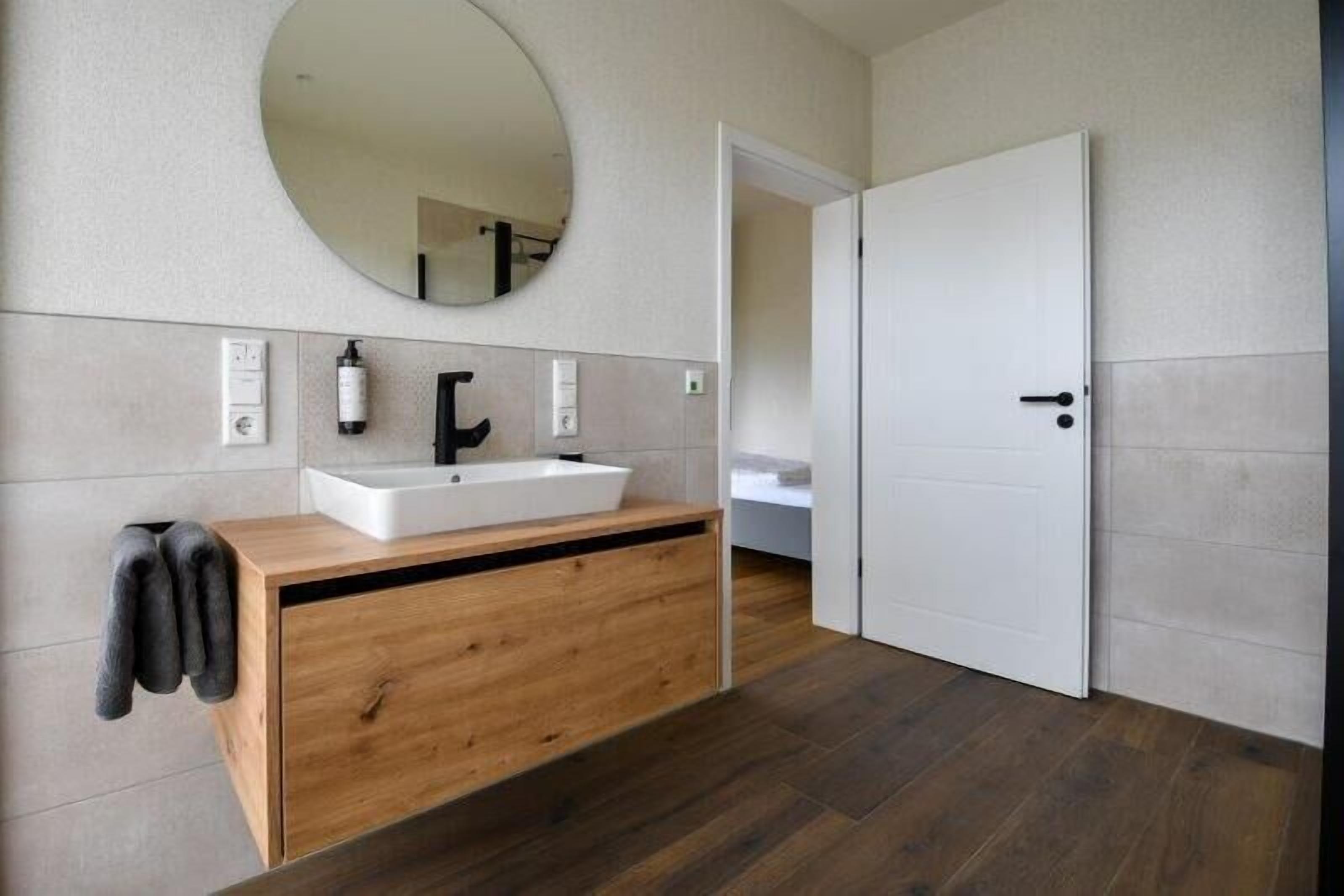 Ein modernes Badezimmer mit Waschtisch aus Holz, einem großen Spiegel und einer weißen Tür.