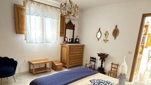 Une chambre à coucher avec un grand lit, une commode en bois, un lustre et une fenêtre avec des rideaux.