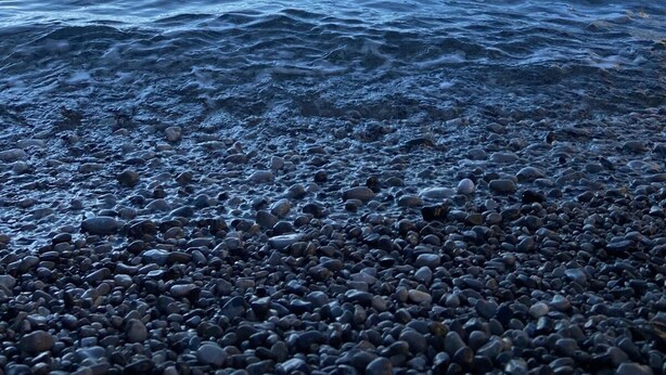 Une plage de galets bordée par une mer calme, avec une structure côtière visible au loin.
