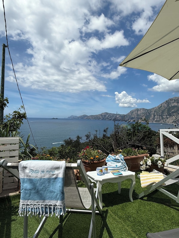 Eine Terrasse mit Blick auf das Meer, ein Stuhl mit Handtuch und Kübelpflanzen.