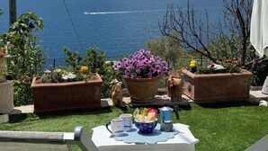 Une terrasse avec une table dressée pour deux personnes, entourée de plantes en pot et offrant une vue panoramique sur la mer et les îles lointaines.
