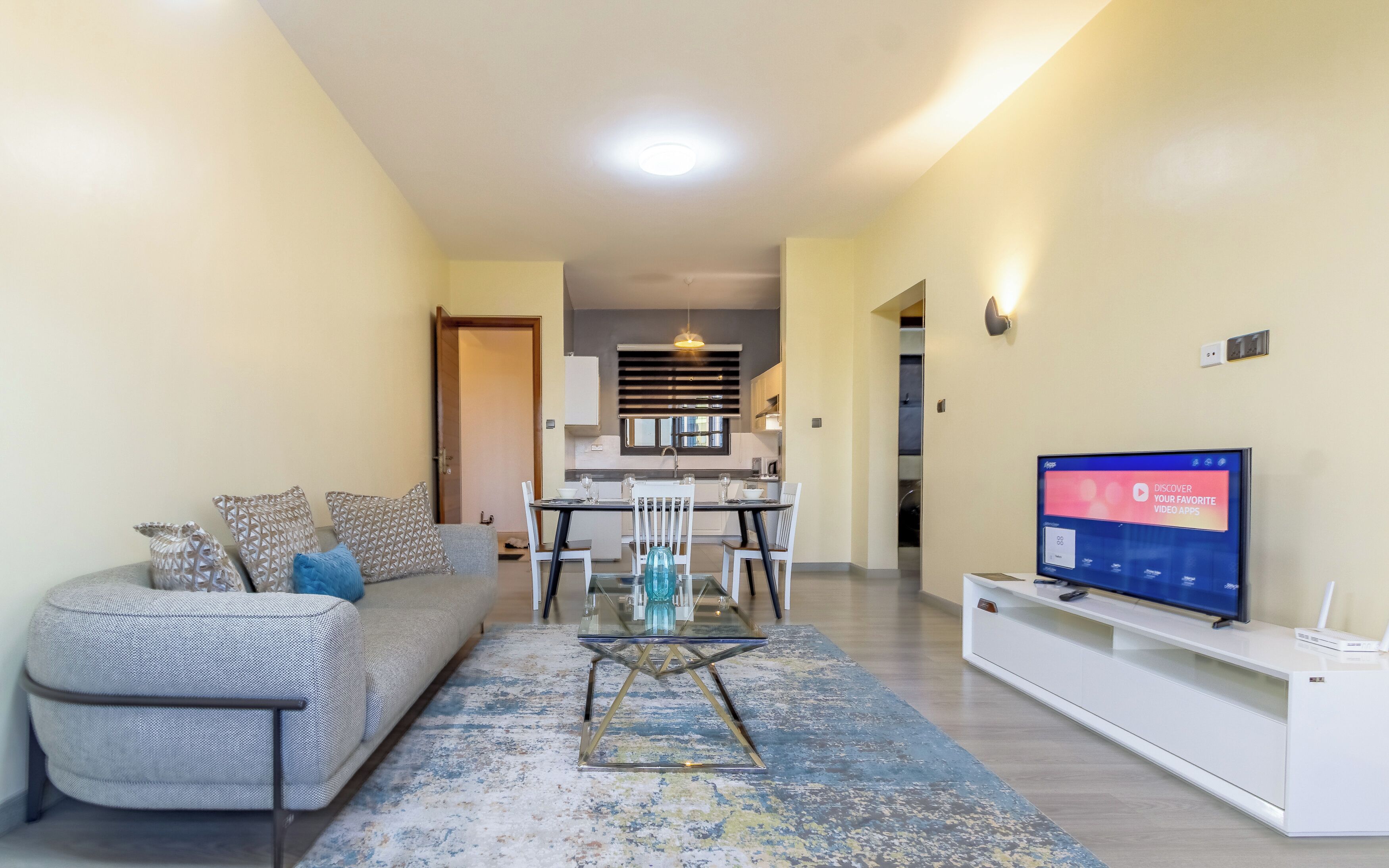 A living room with a sofa, coffee table, TV, and a dining area with chairs and a table.