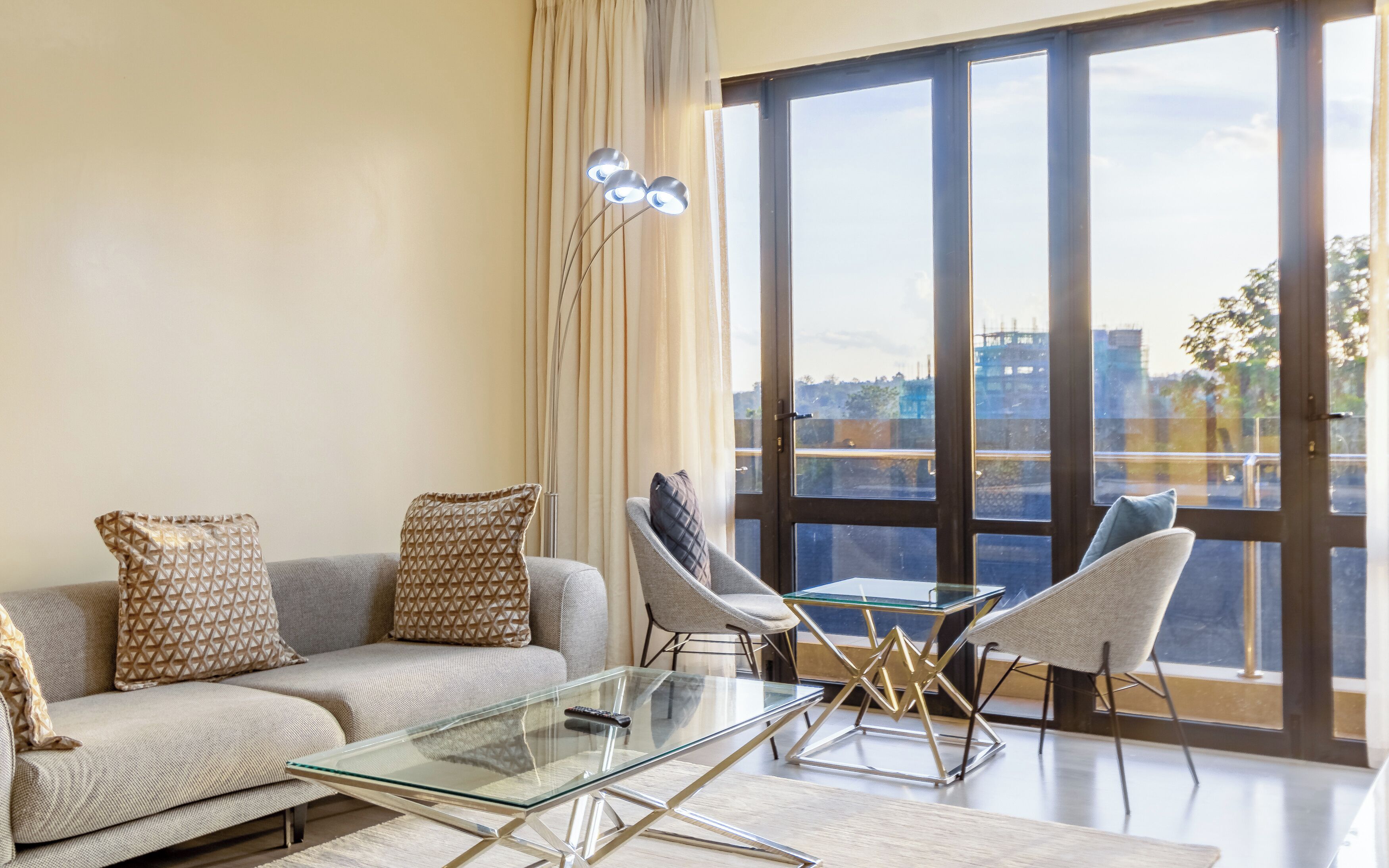 Een moderne woonkamer met een bank, twee fauteuils, een glazen salontafel en een grote schuifpui naar een buitenbalkon.