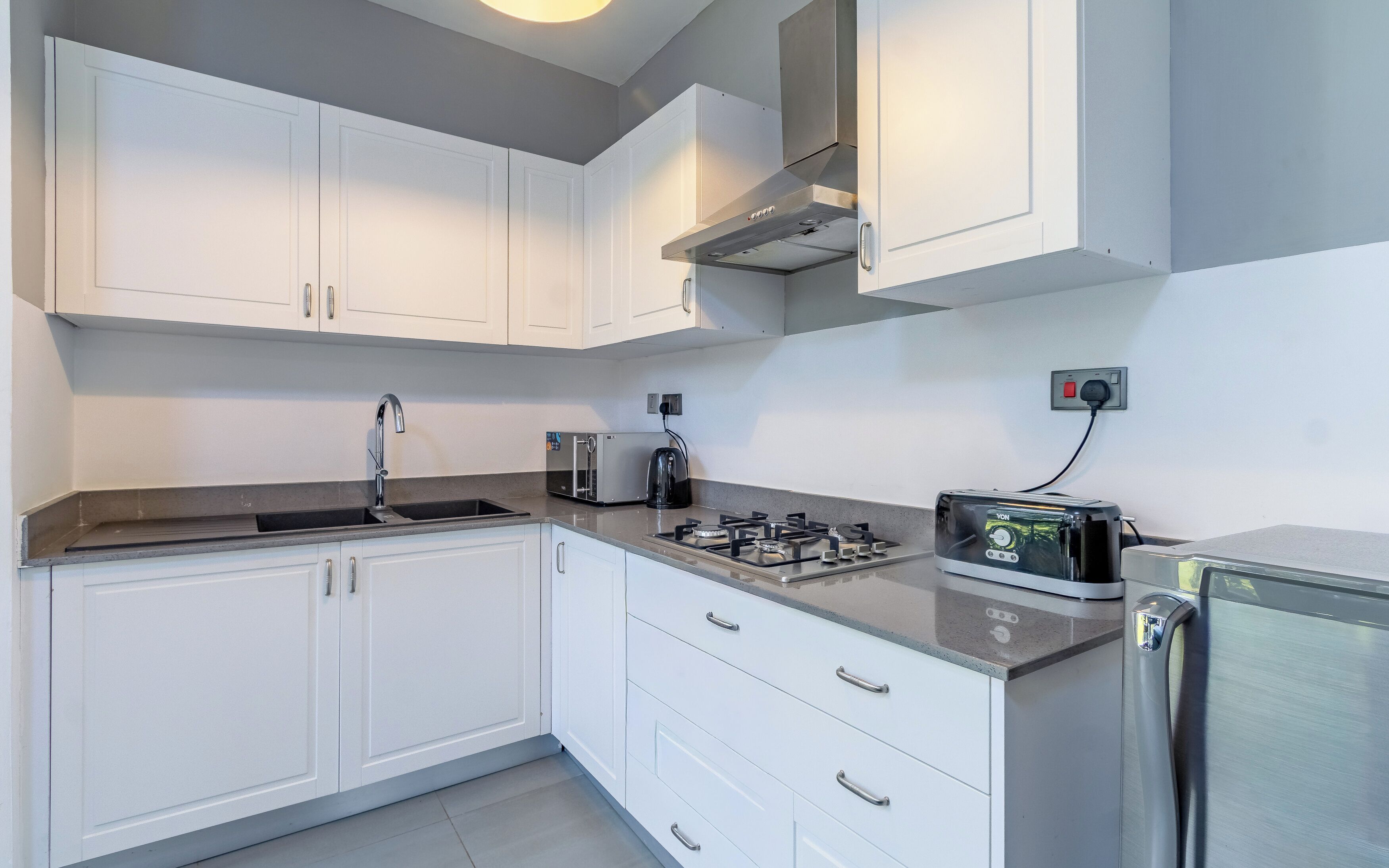 Una cocina moderna con armarios blancos, estufa de acero inoxidable, tostadora y tetera.