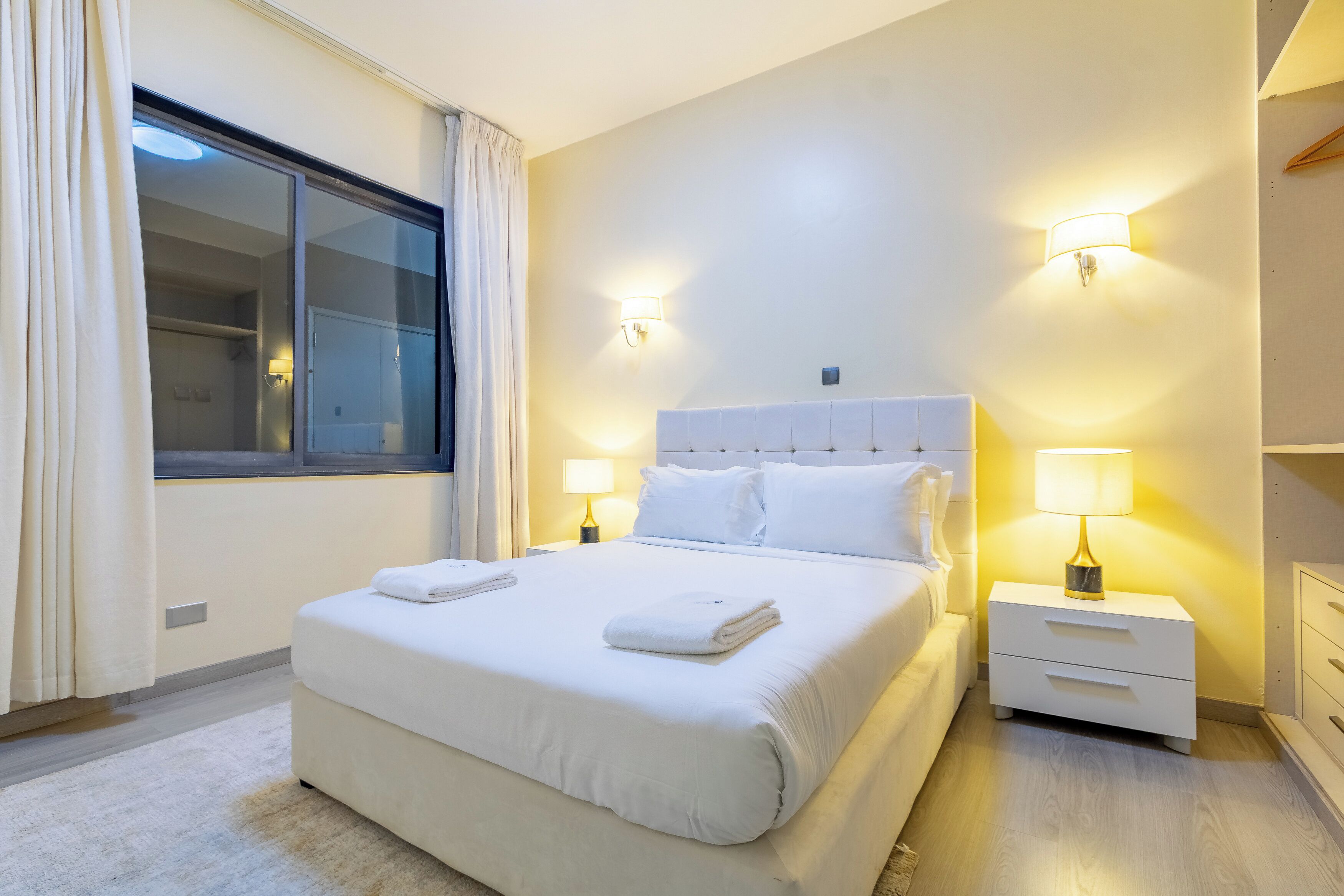 A hotel room with a large bed, two bedside lamps, a nightstand, and a window with curtains.