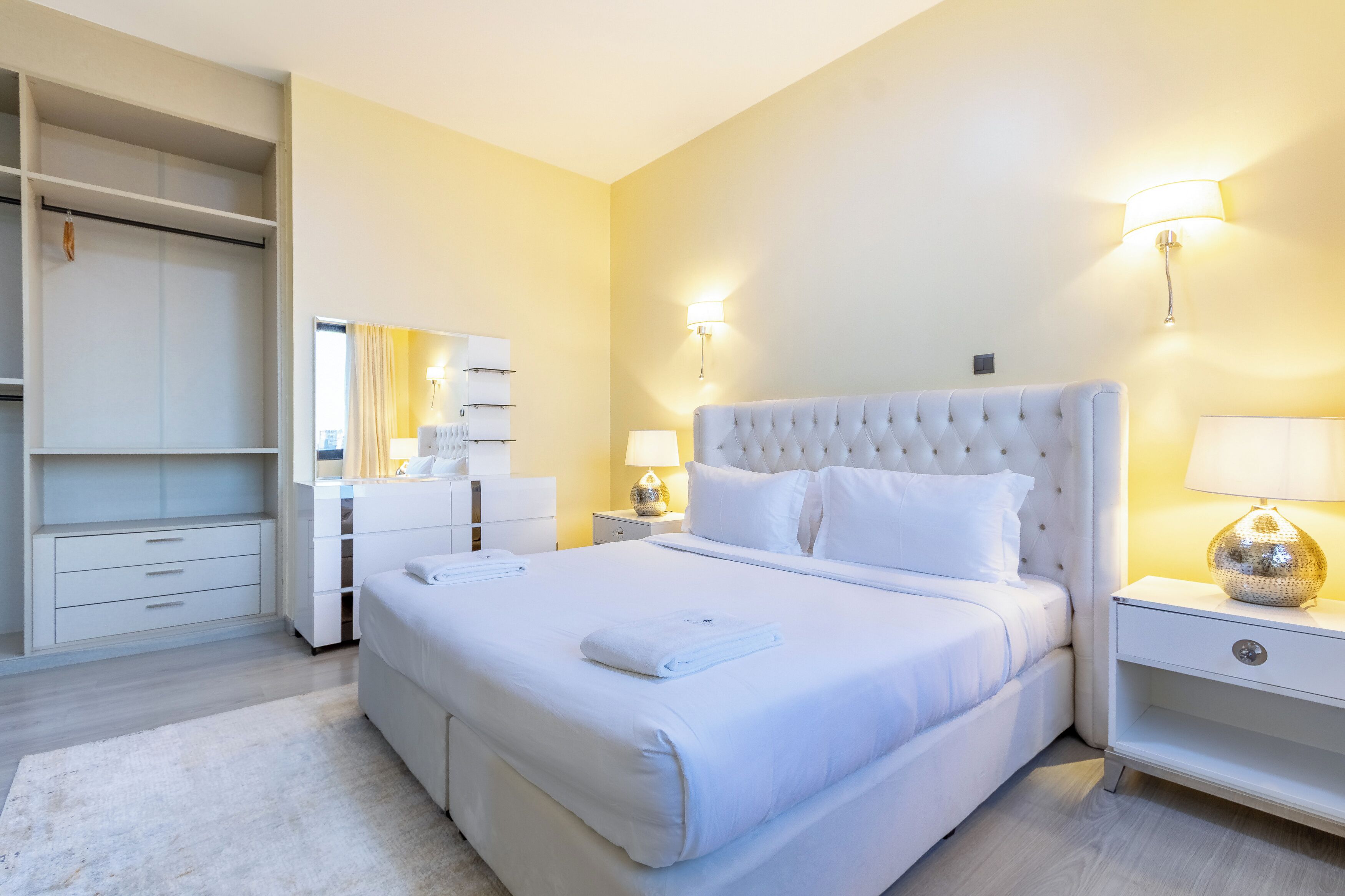 A neatly arranged bedroom with a large bed, bedside tables, a wardrobe, and a mirror.