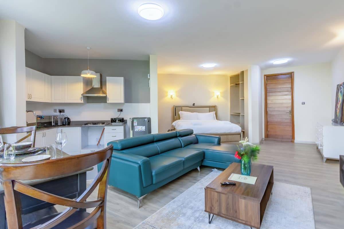A modern hotel room with a kitchenette, a sofa, a dining area, and a bed.