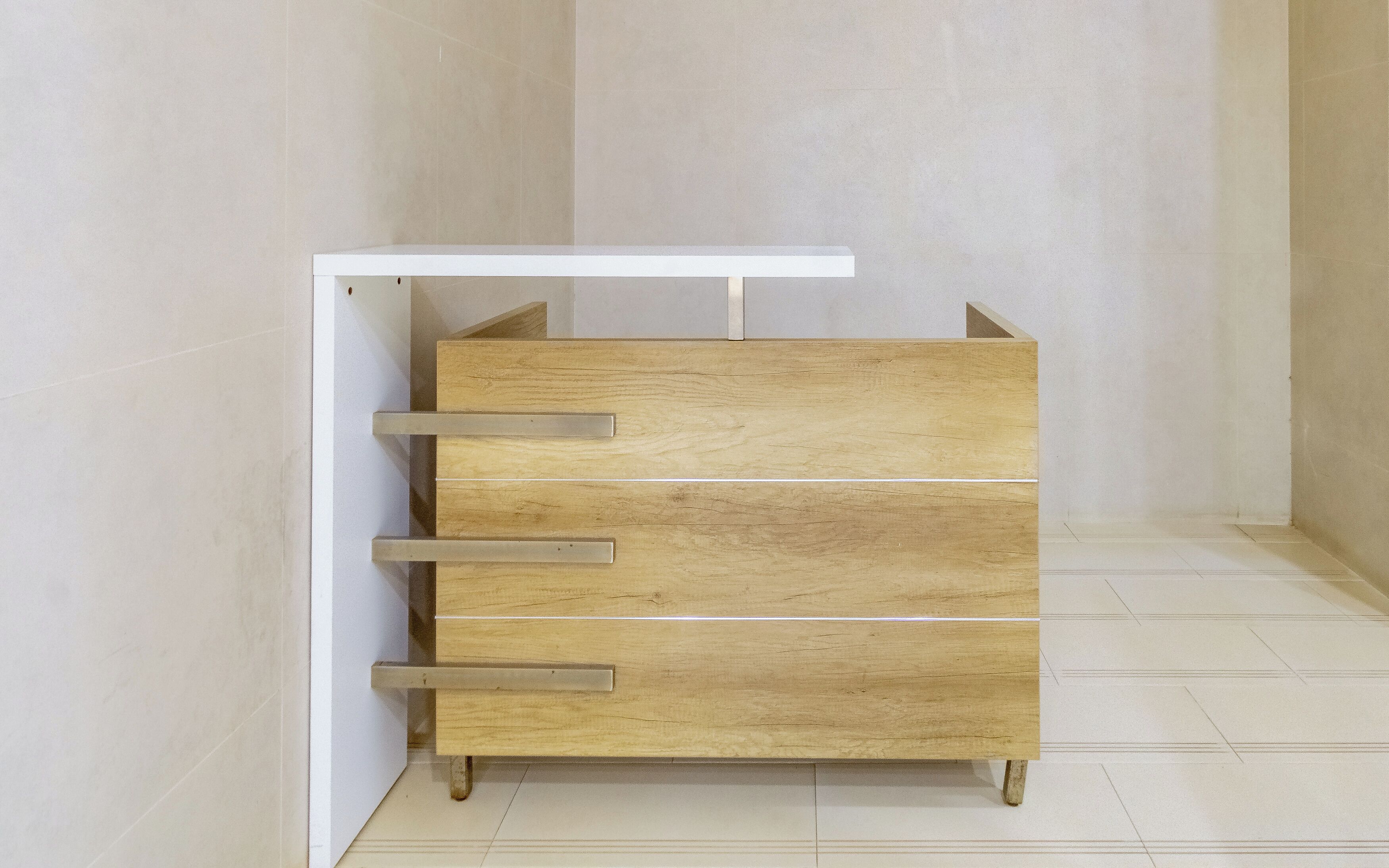 Un aparador de madera con cajones y un estante, colocado contra una pared en una habitación con suelo de baldosas.