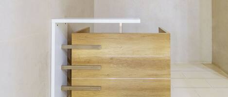 A wooden dresser with drawers and a shelf, positioned against a wall in a room with tiled flooring.