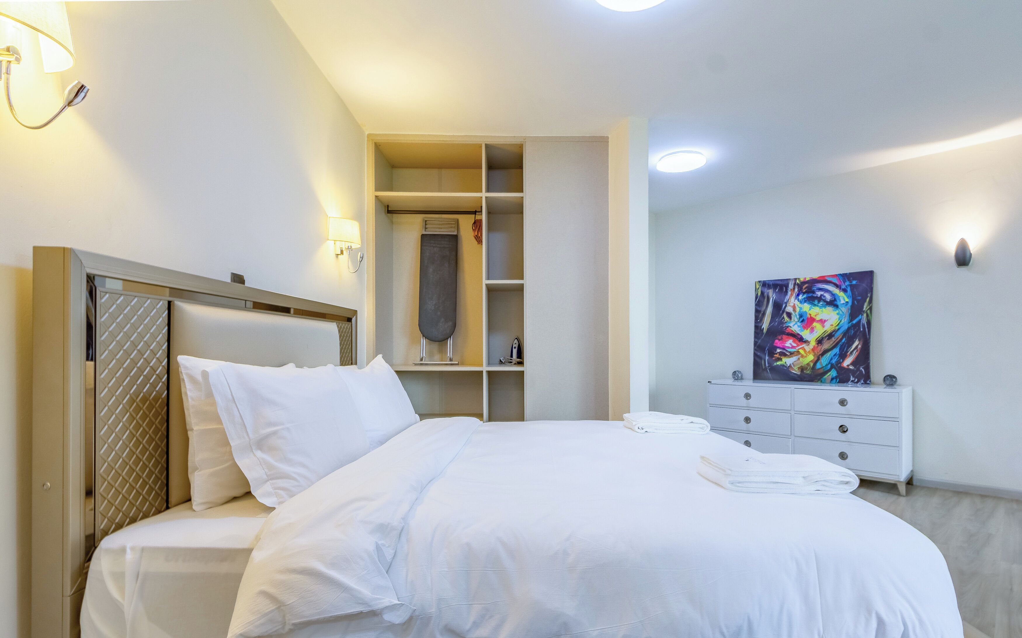 A bedroom with a bed, a wardrobe, a dresser, and a painting on the wall.