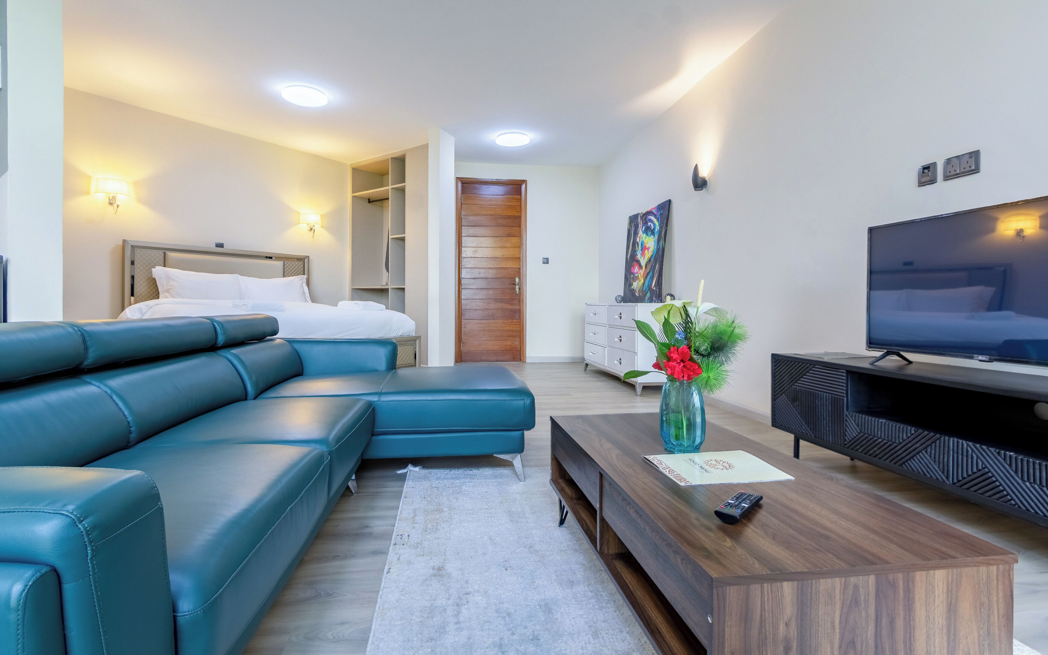 Ein modernes Hotelzimmer mit Sofa, Fernseher, Holzschrank und einer Tür zu einem Kleiderschrank.