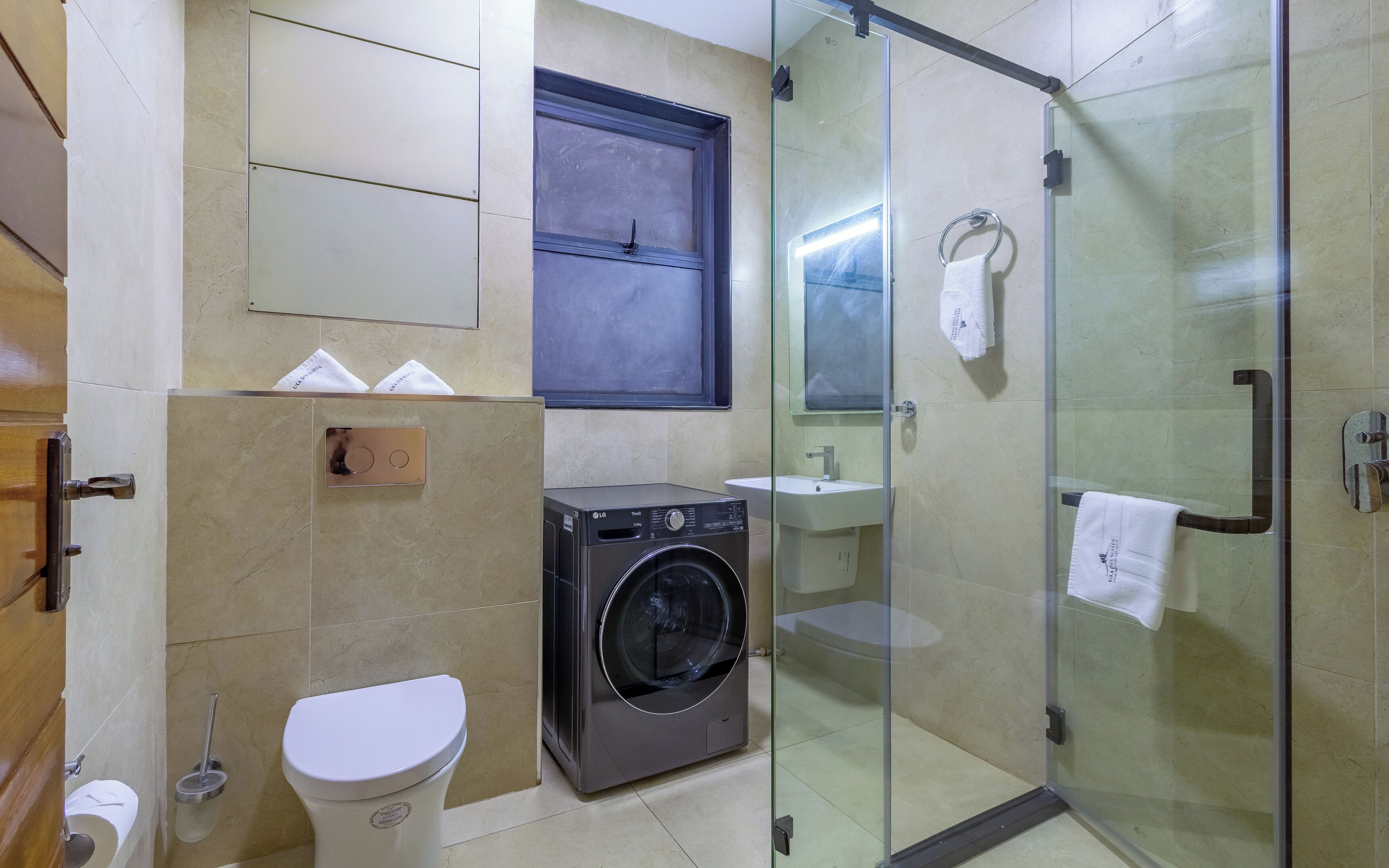 A bathroom with a toilet, washing machine, glass shower enclosure, and a sink.