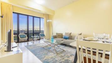 Ein modernes Wohnzimmer mit Sofa, Glastisch, Esstisch und großem Fenster mit Blick auf die Stadt.