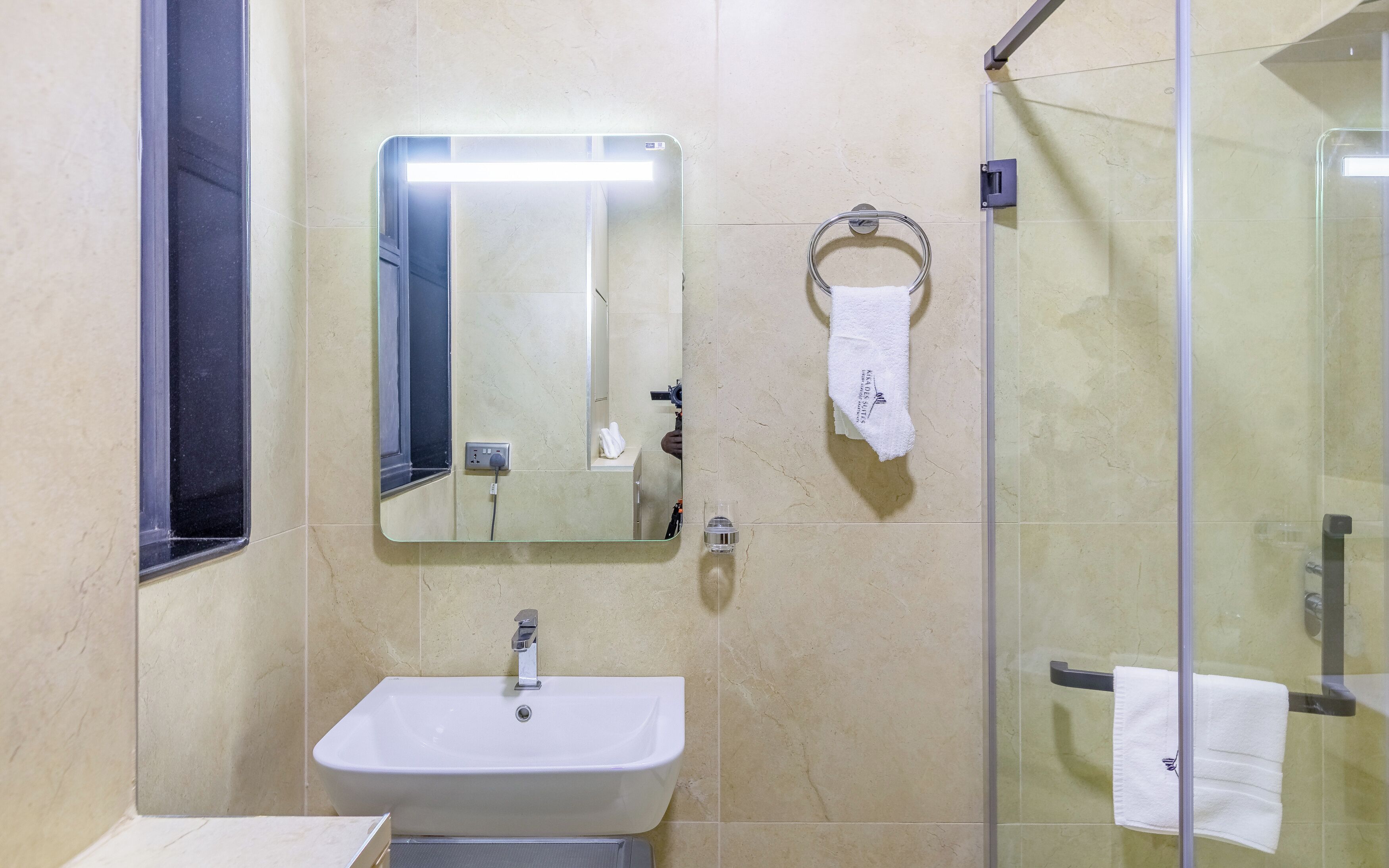 Ein Badezimmer mit Waschbecken, Spiegel, Handtuchhalter und Duschkabine.