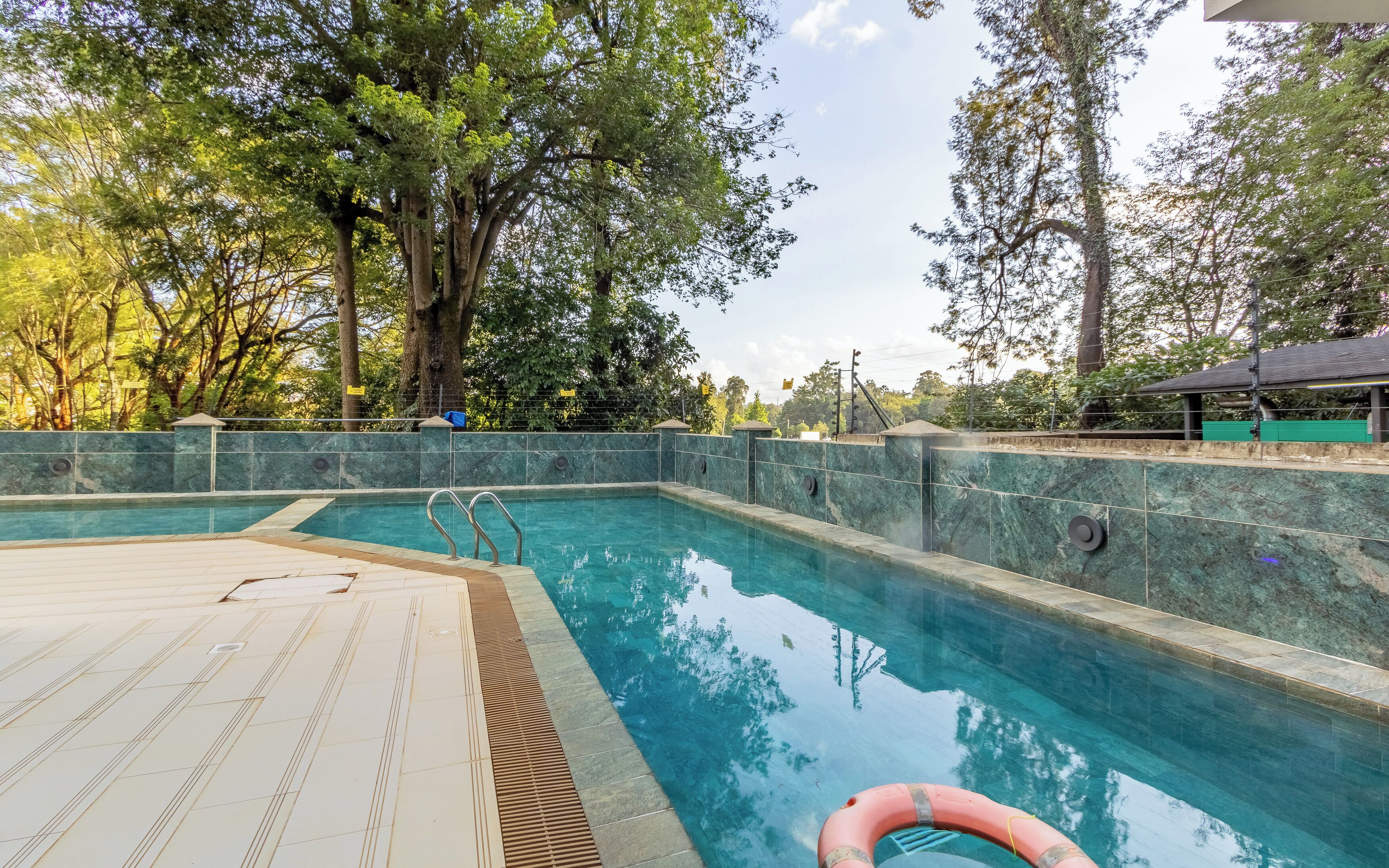 Una piscina con cubierta de baldosas, rodeada de árboles y un muro de piedra.