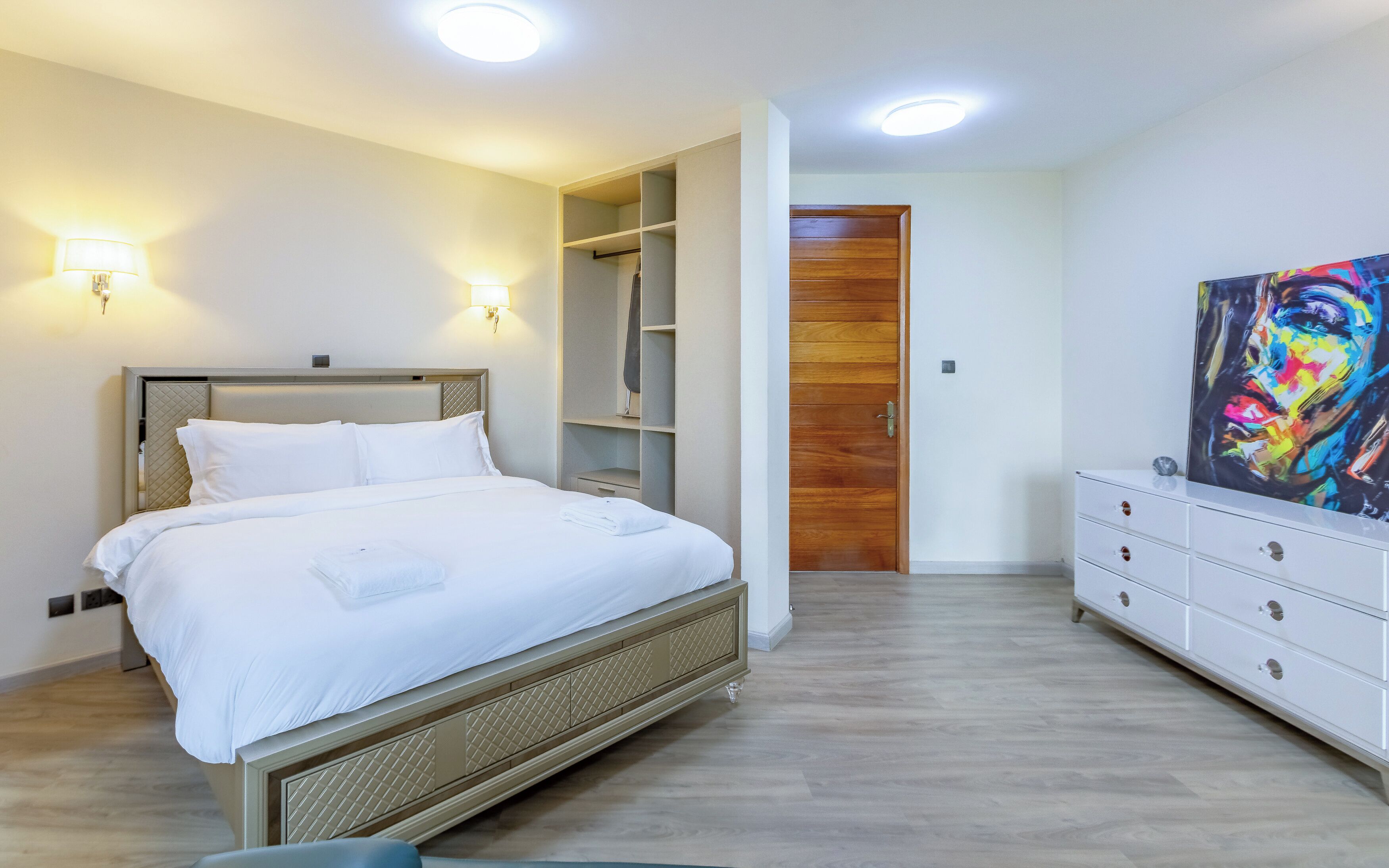 Une chambre d’hôtel avec un lit, des lampes de chevet, une armoire, un tableau et une porte en bois.
