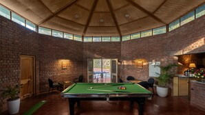 Una sala de billar con mesa de pool, sillas y pared de ladrillo.
