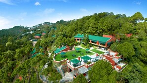 Un hotel en una ladera con varias construcciones, un césped cuidado y un bosque denso que rodea la propiedad.