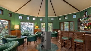 Un interior acogedor con una zona de bar, sillas tapizadas de verde y una chimenea central.