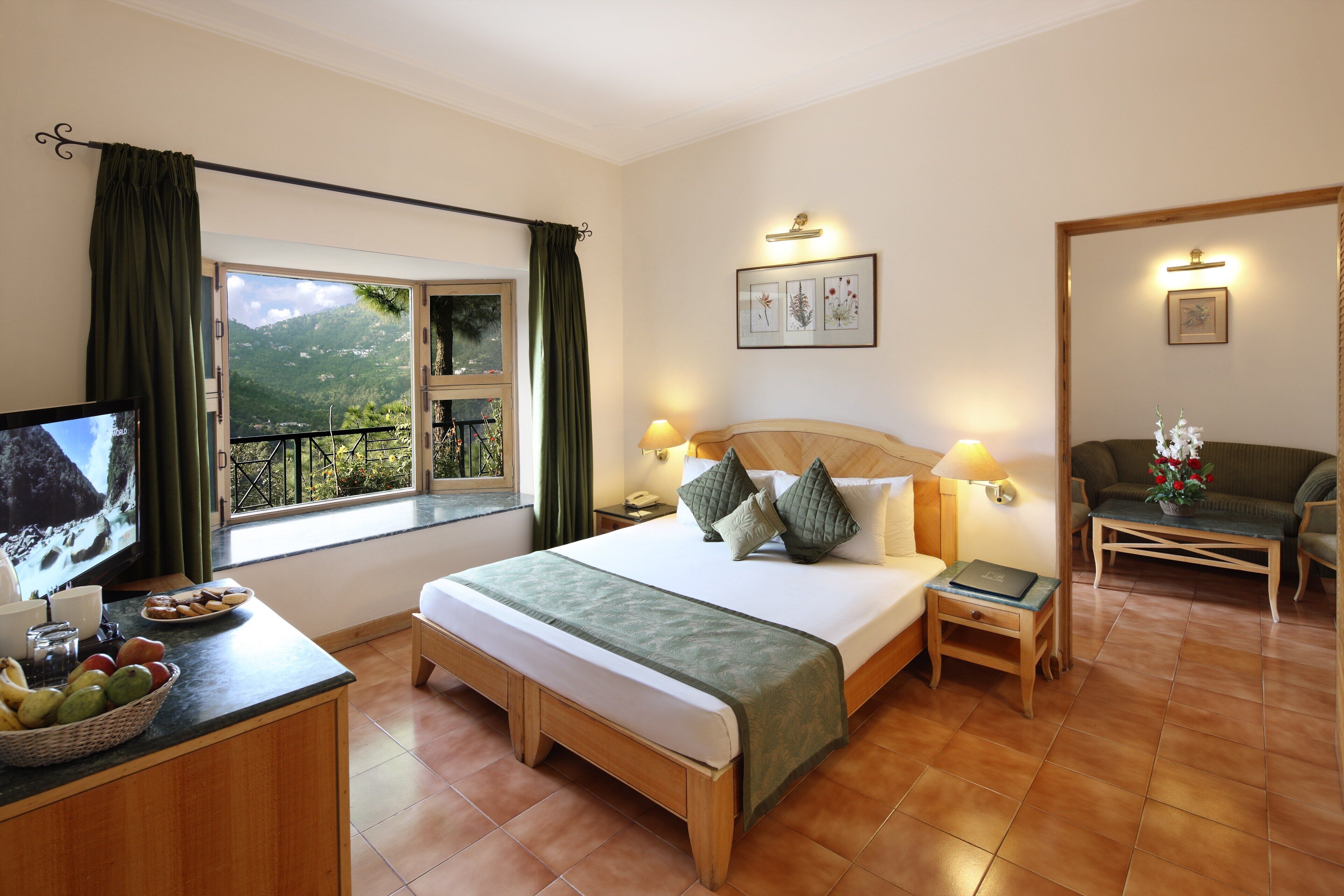 Een hotelkamer met een bed, nachtkastjes, een televisie, een raam met gordijnen en een balkon met uitzicht op de bergen.