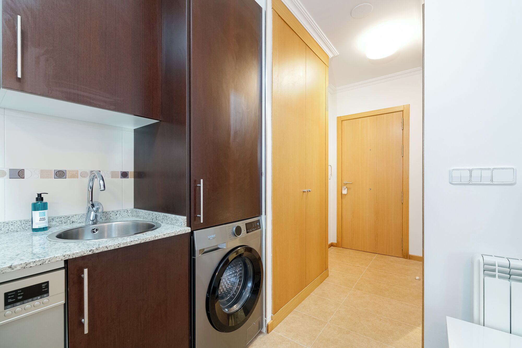 Una cocina compacta con lavadora, un lavabo y armarios de madera.
