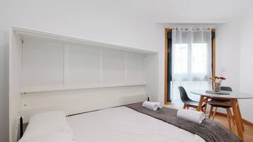 Habitación de hotel con cama, una mesita redonda con un florero y una ventana con cortinas traslúcidas.