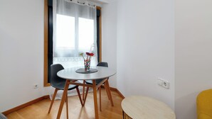 Ein Essbereich mit einem runden Tisch, zwei Stühlen, einer Blumenvase und einem Fenster mit transparenten Vorhängen.