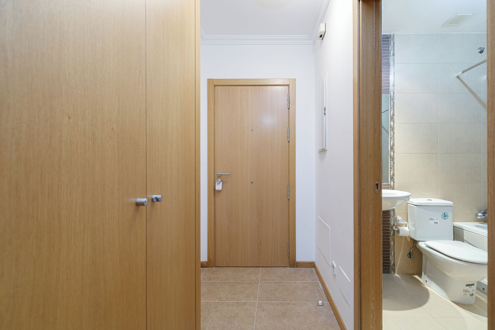 Un pasillo estrecho que conduce a un baño con inodoro, lavabo y zona de ducha.