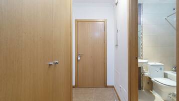Un pasillo estrecho que conduce a un baño con inodoro, lavabo y zona de ducha.