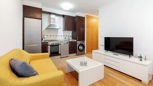 Ein kompakter Wohnbereich mit Sofa, Couchtisch, Fernseher, Waschmaschine und Küchenzeile.